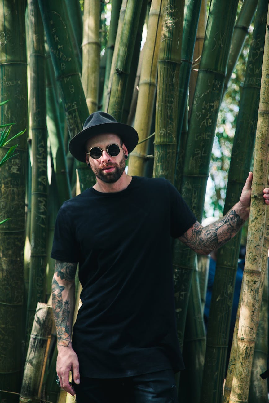 man holding bamboo plant wearing sunglasses and fedora hat